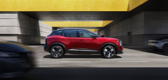 Nissan Kicks 2026 rojo con techo negro visto de perfil, en movimiento bajo una estructura de concreto con paneles amarillos